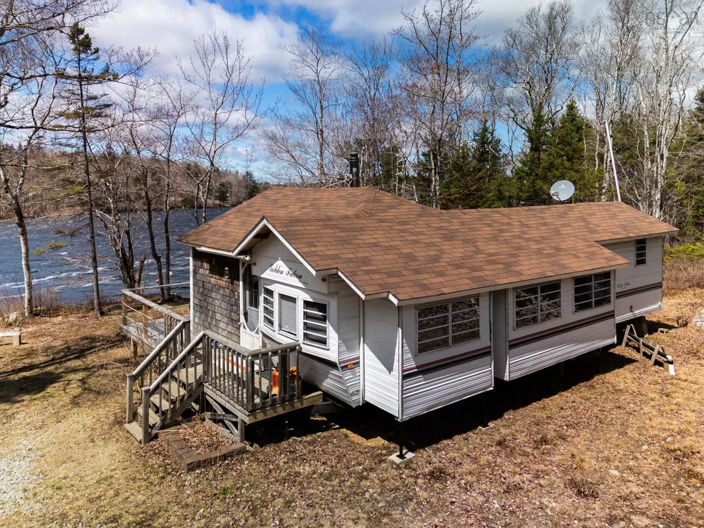 Exterior view of "Golden Salmon" cabin with brown roof, white siding, and wooden deck, near a river and trees.