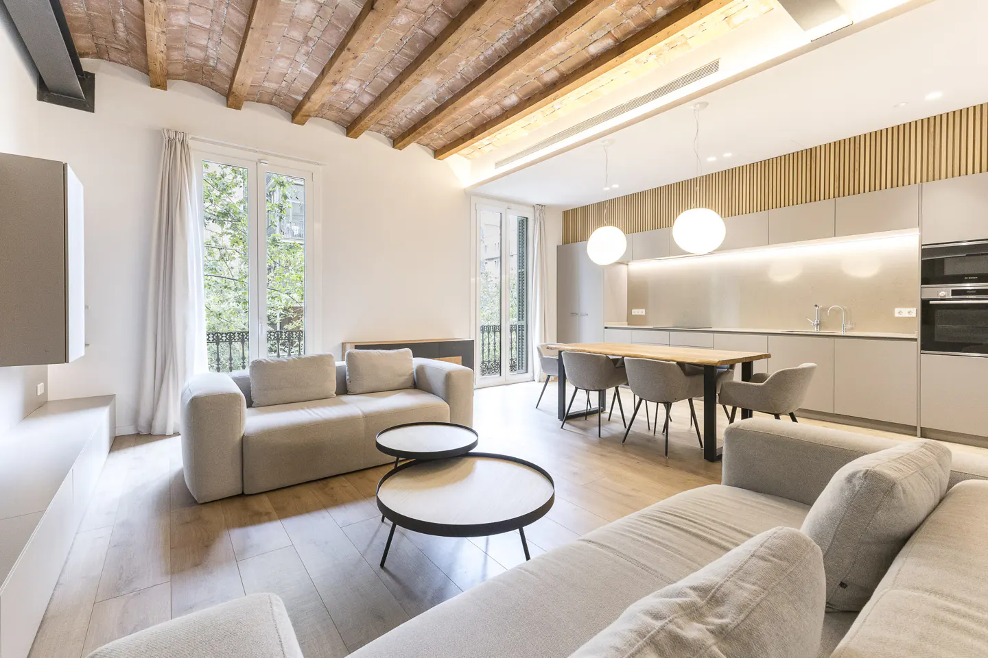 Open-concept living space with light gray sofas, round tables, and a modern kitchen with a wood dining table.