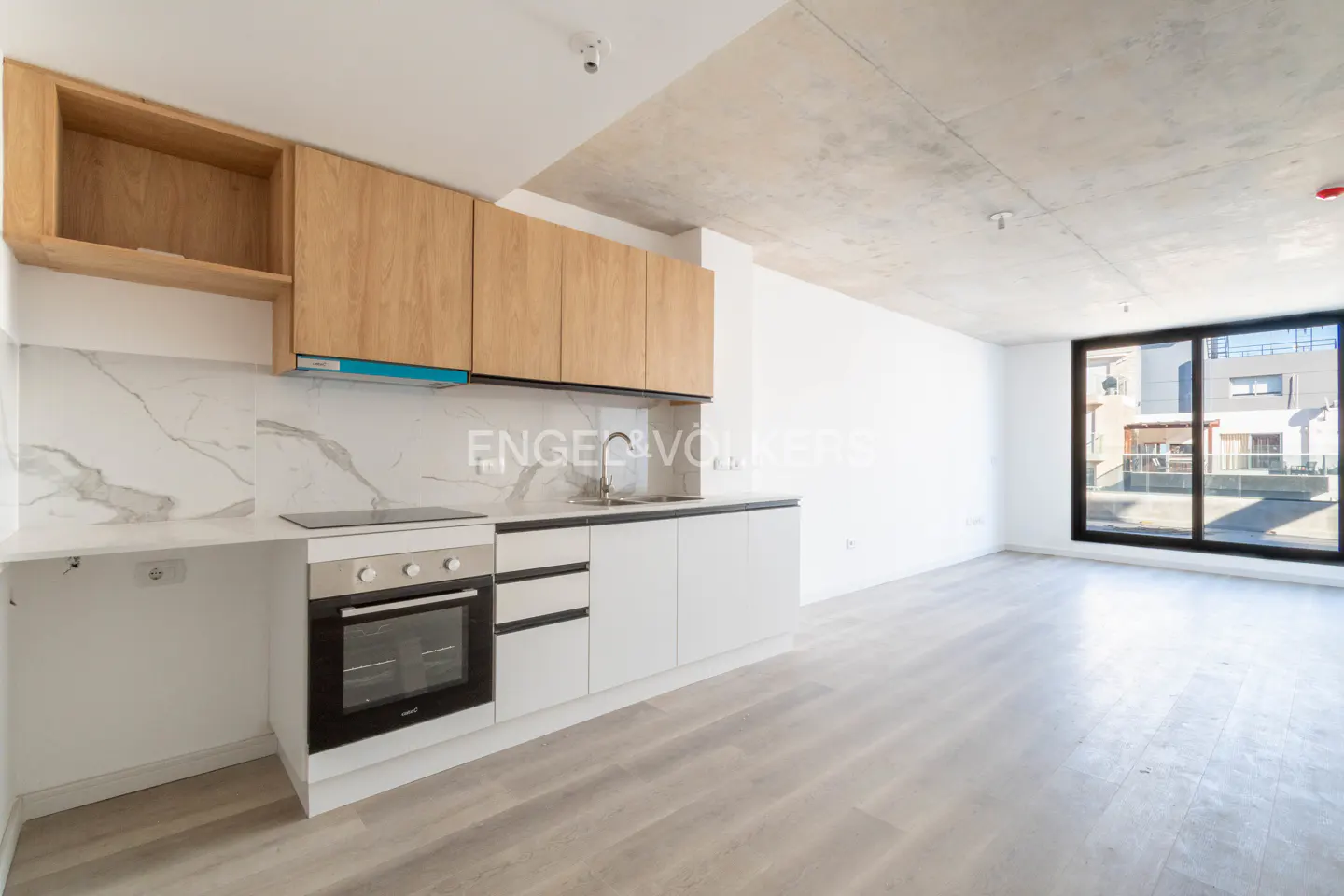 A modern kitchen with wood cabinets, white countertops, and stainless steel appliances in a bright, open-concept space.