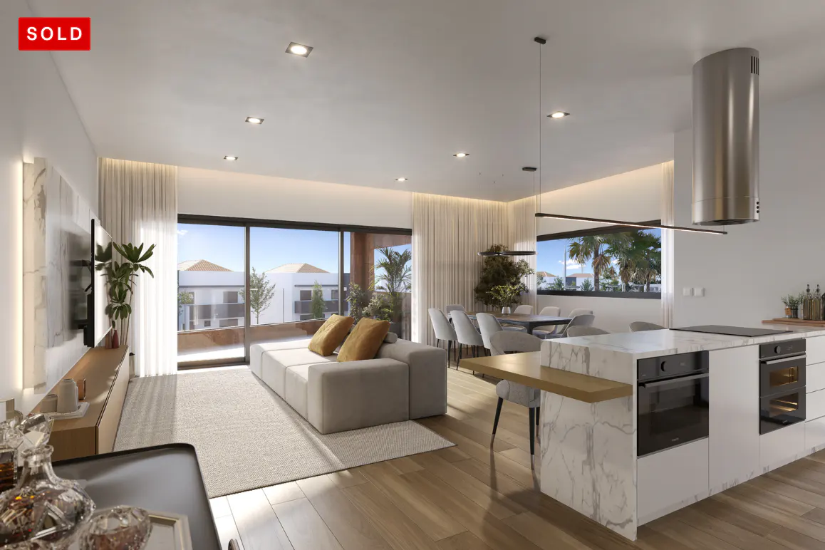 Bright, modern open-plan living space with a white sofa, kitchen island, dining table, and large windows. "SOLD" in red in the upper left corner.