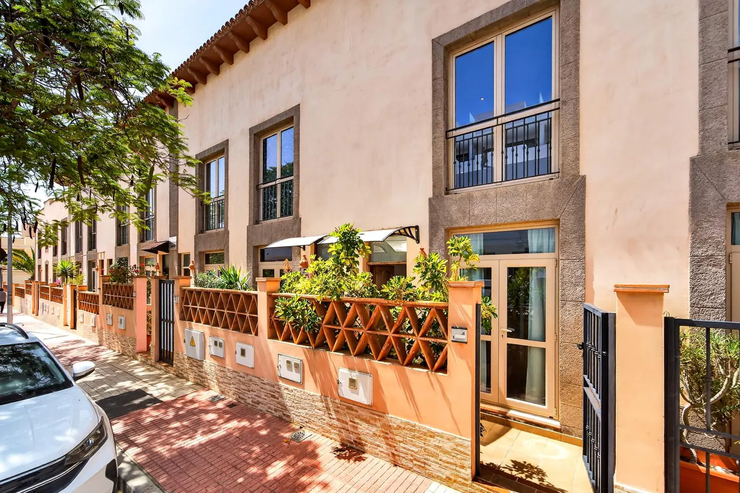 Row of peach townhouses with brown trim, decorative fences, and green plants along a brick sidewalk.