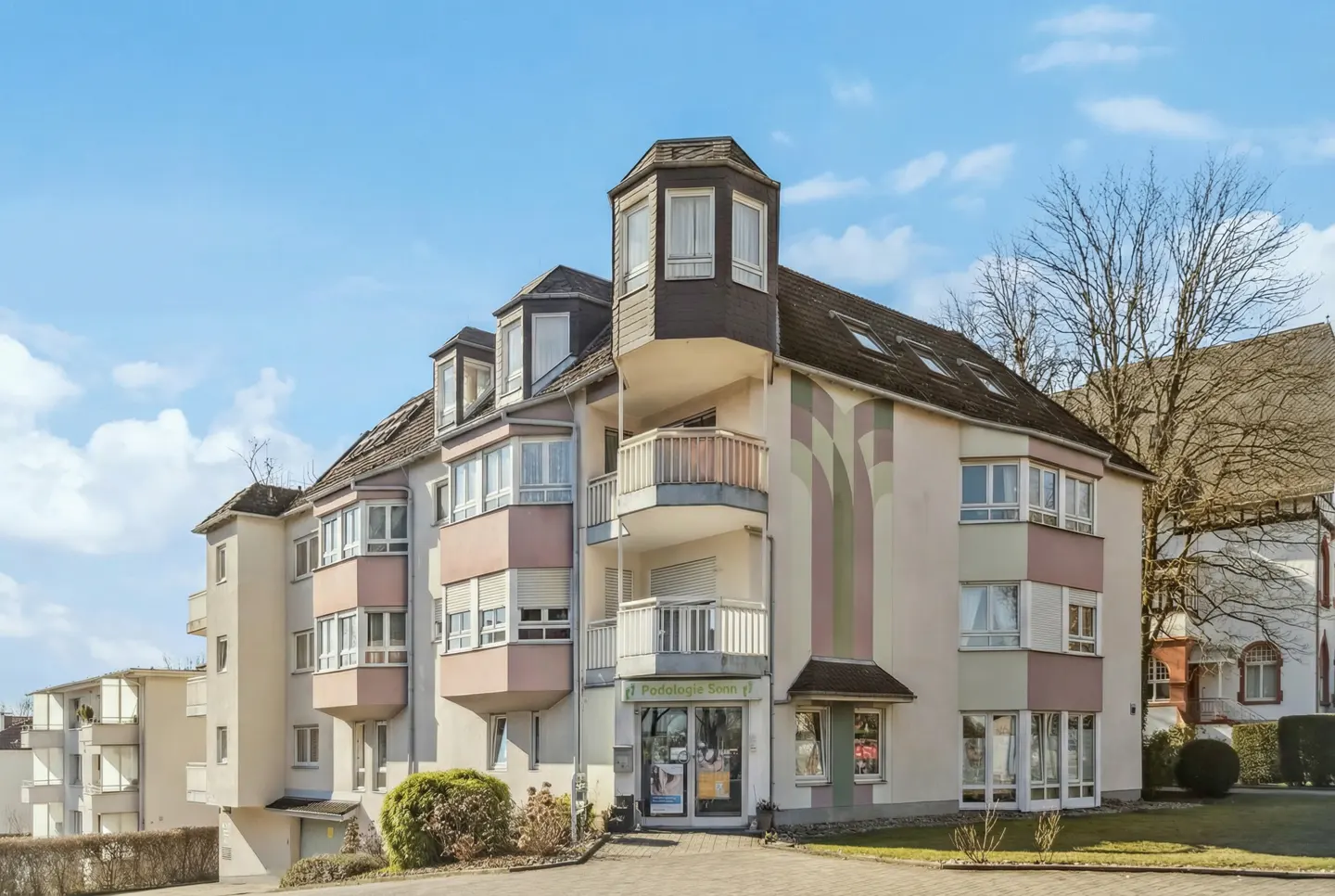 Exterior view of a multi-story apartment building with balconies and a shopfront, under a blue sky.