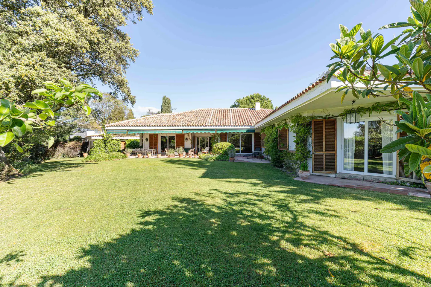 Exterior view of a one-story house with a red tile roof and a large green lawn on a sunny day.