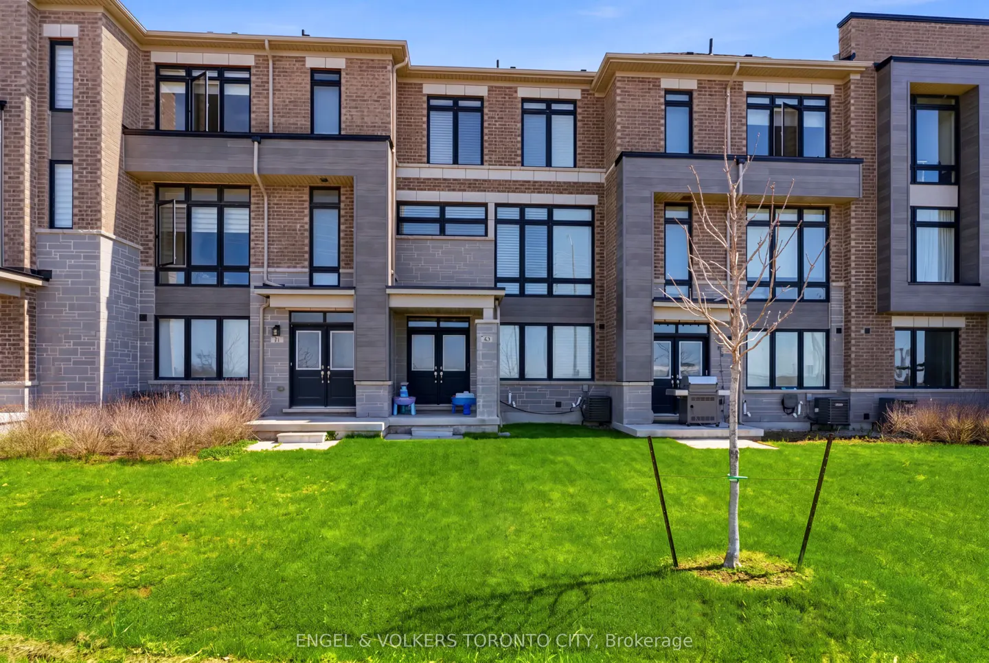 Exterior view of a three-story brick townhouse with black windows and a green lawn.