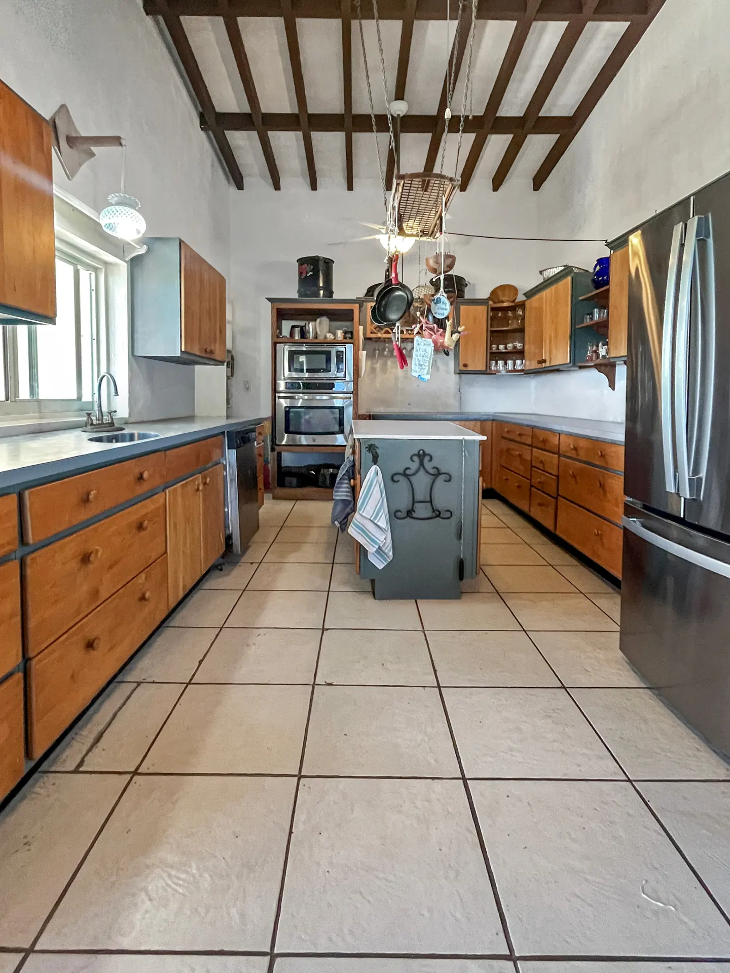 A kitchen with wood cabinets, a gray island, and stainless steel appliances. Pots hang from a rack above the island.