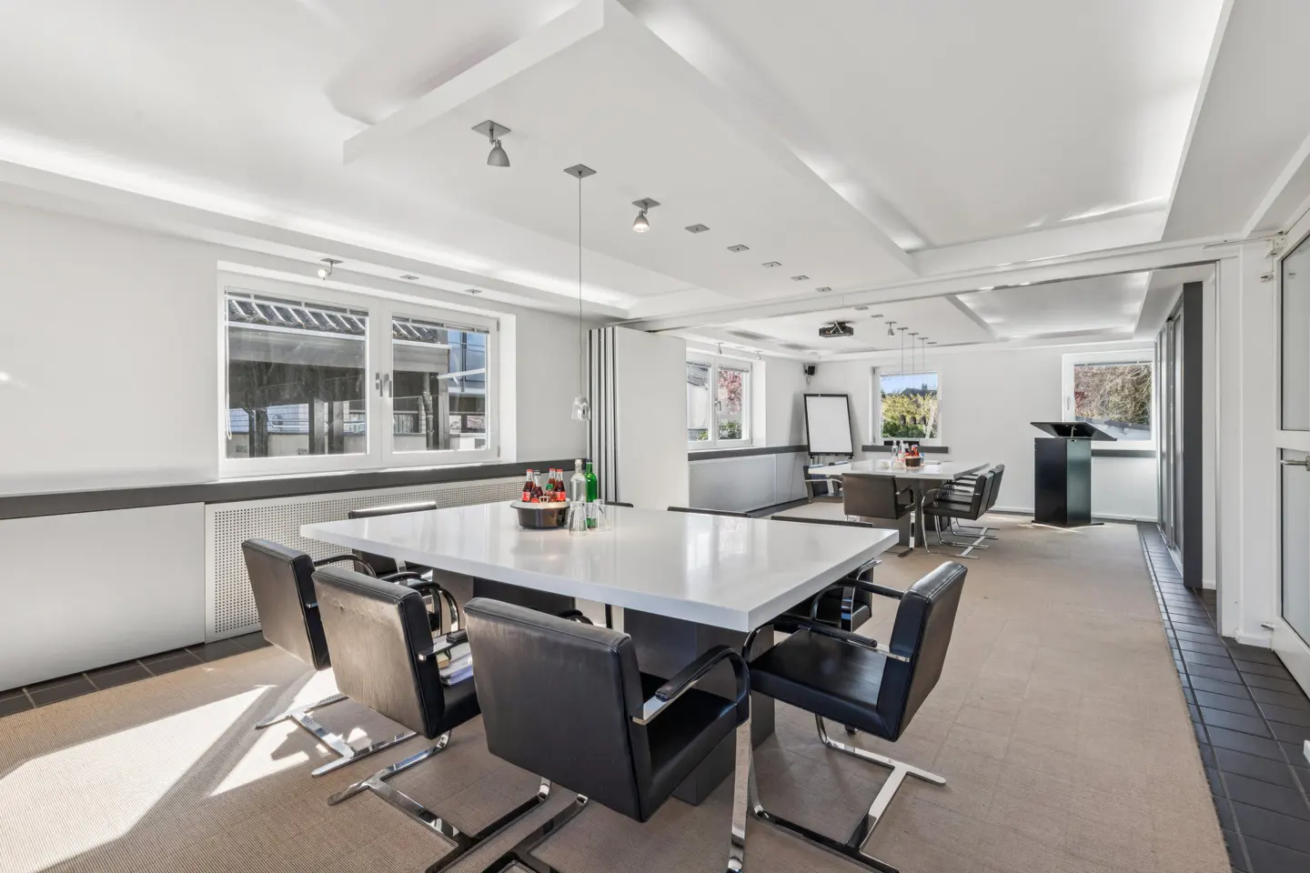 Bright conference room with a large white table, black chairs, and a projector on the ceiling.
