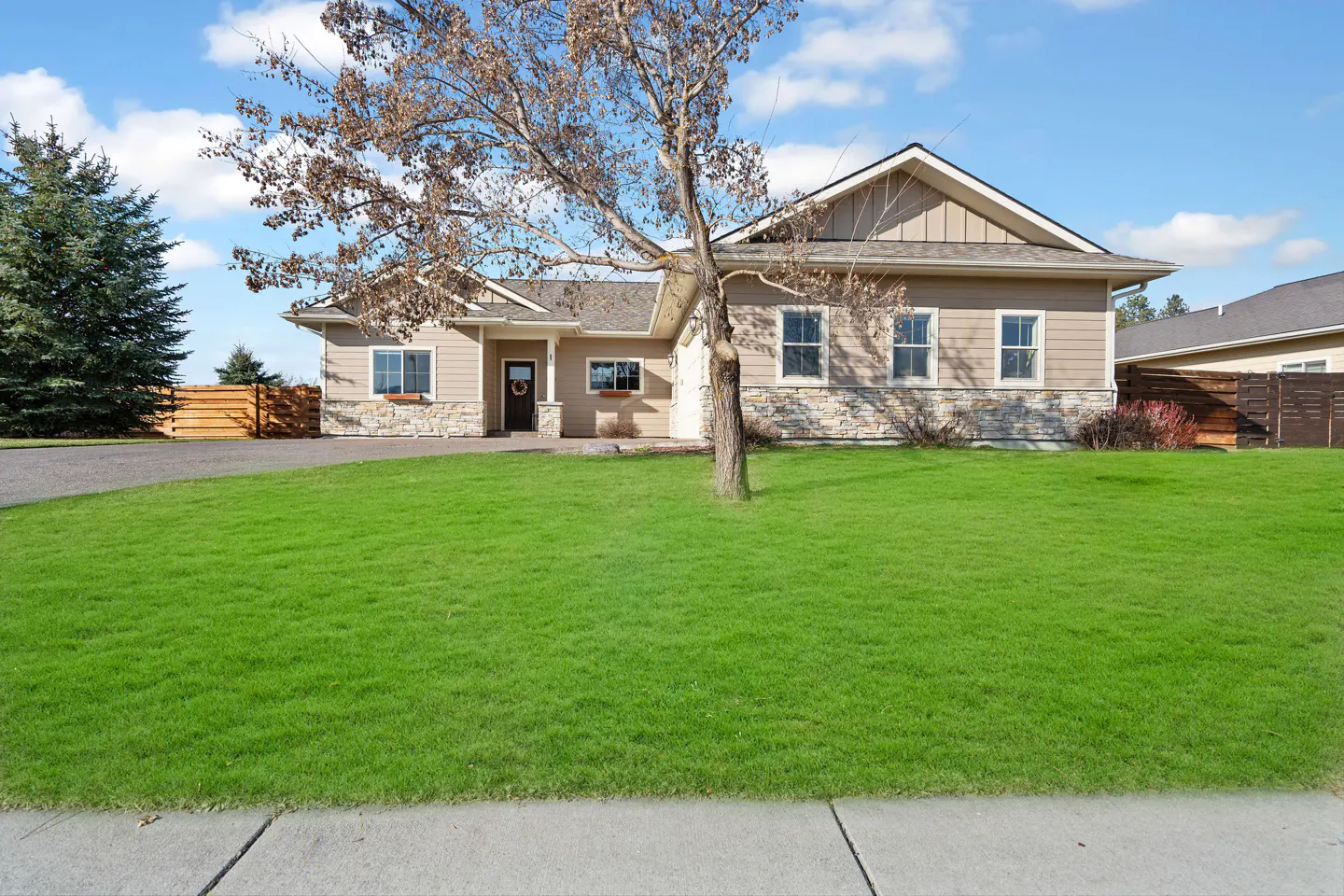 A tan single-story house with a stone foundation and a large green lawn on a sunny day.