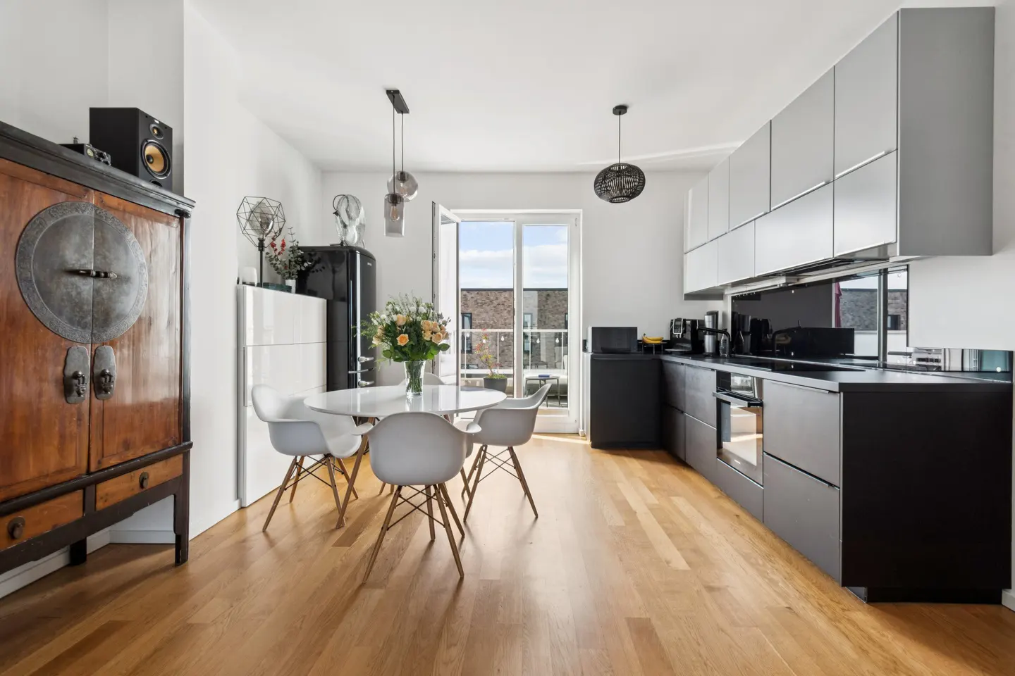 A modern kitchen with light wood floors, a round white table with chairs, and black and gray cabinets.