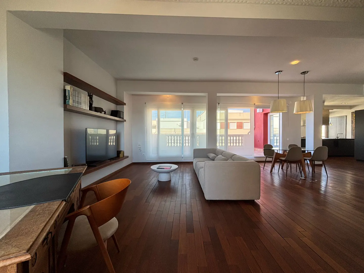 Bright, open-concept living space with hardwood floors, white walls, and a large white sofa. A dining table and chairs are visible in the background.