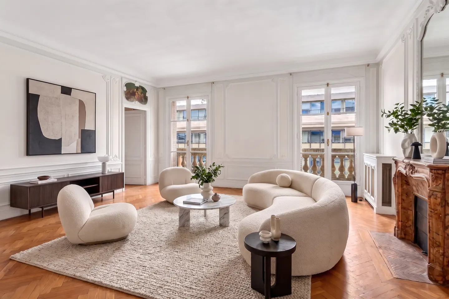 Bright living room with cream curved sofa and chairs, marble coffee table, wooden floors, and a fireplace.