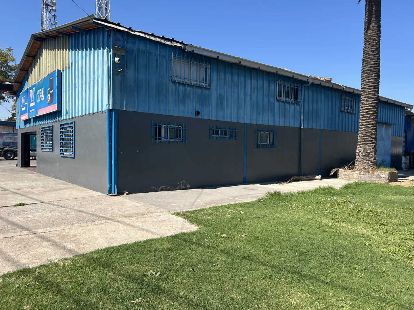 Exterior view of a two-story blue and gray commercial building with barred windows, a sign, and a palm tree.