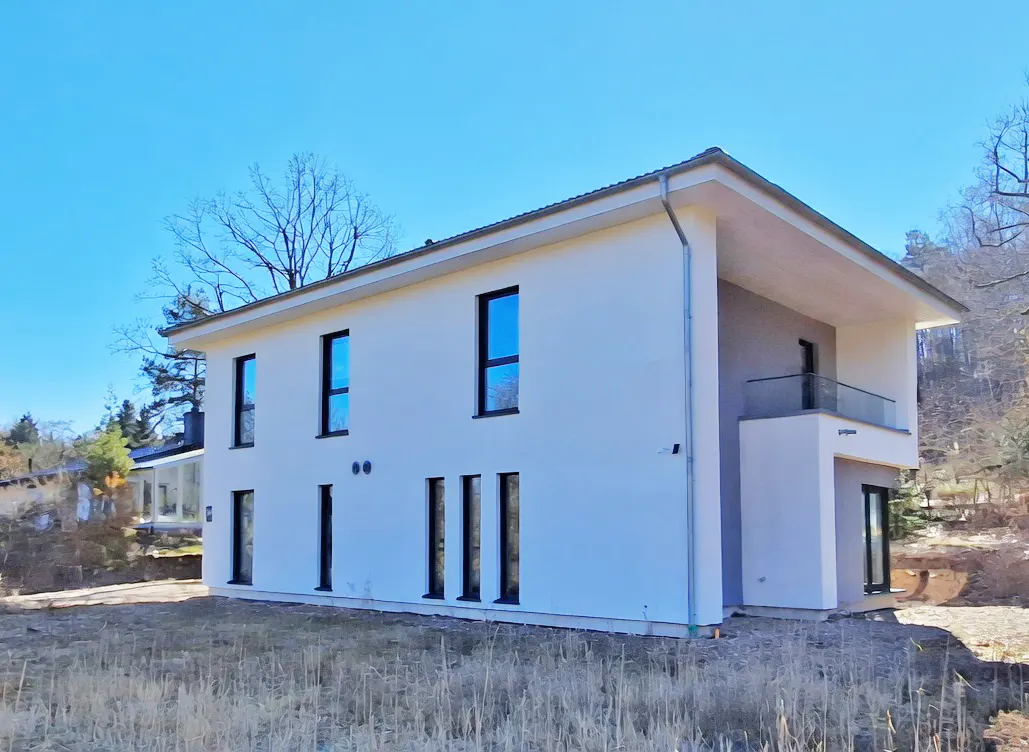 Two-story modern white house with black framed windows and a balcony on a sunny day.