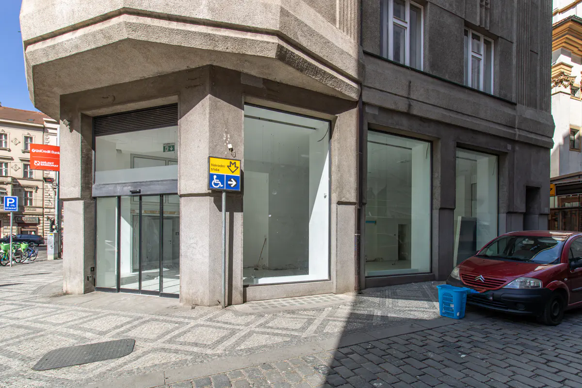 Exterior view of a gray building with large glass windows, a red car parked nearby, and a blue handicap sign.