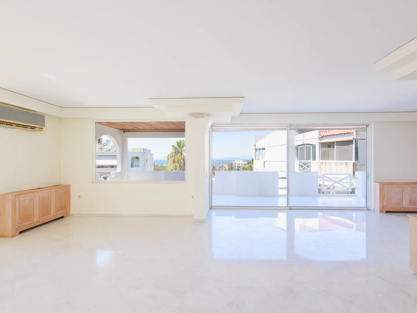 Bright, empty room with white marble floors, light wood cabinets, and large windows with ocean views.