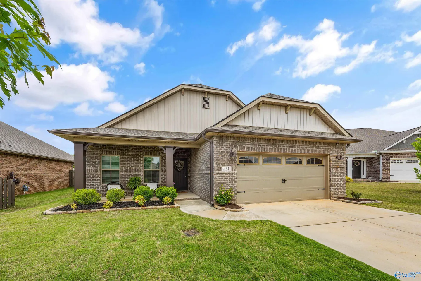 A single-story brick house with a beige garage door, green lawn, and blue sky.