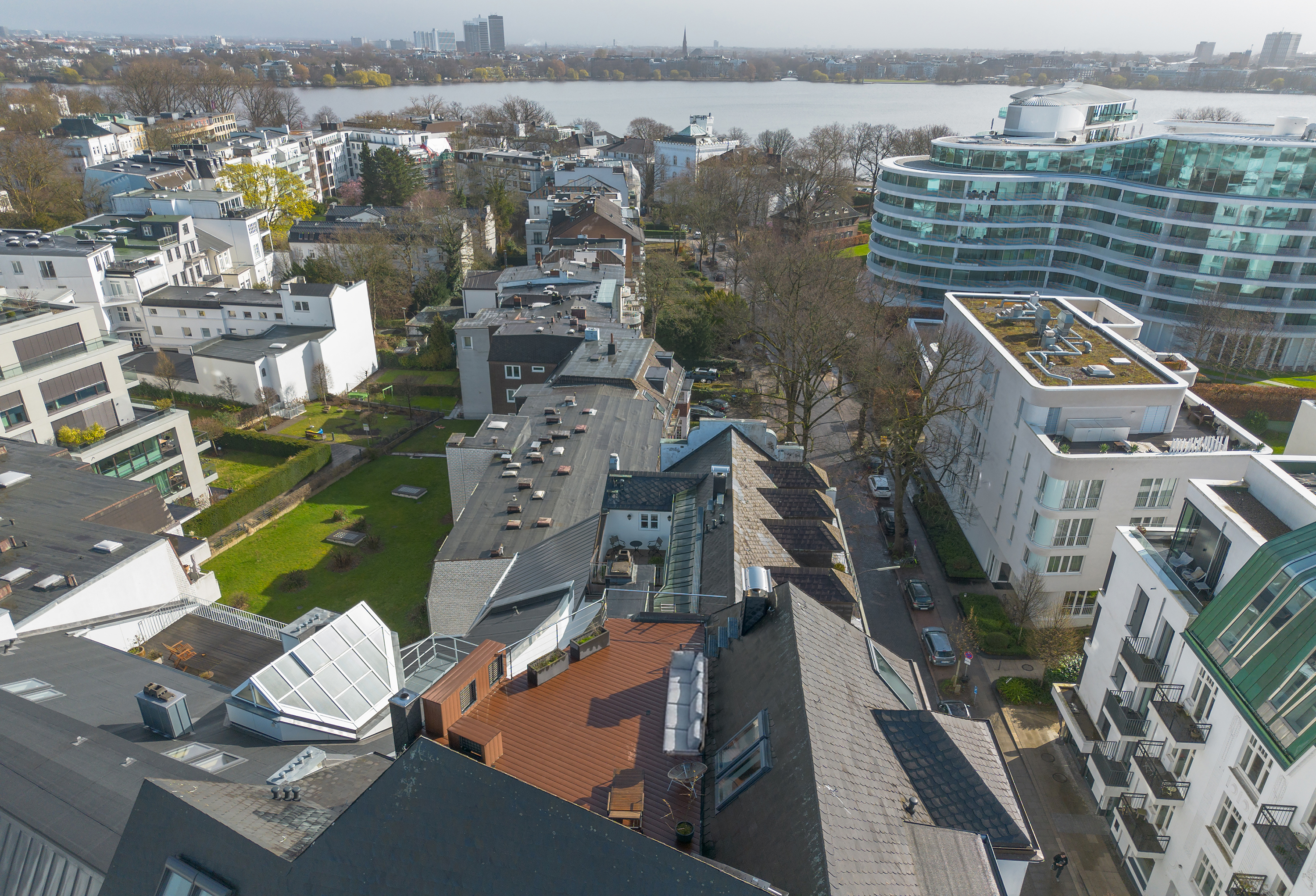 Aerial view of a Hamburg neighborhood with modern buildings, trees, and a lake in the background.