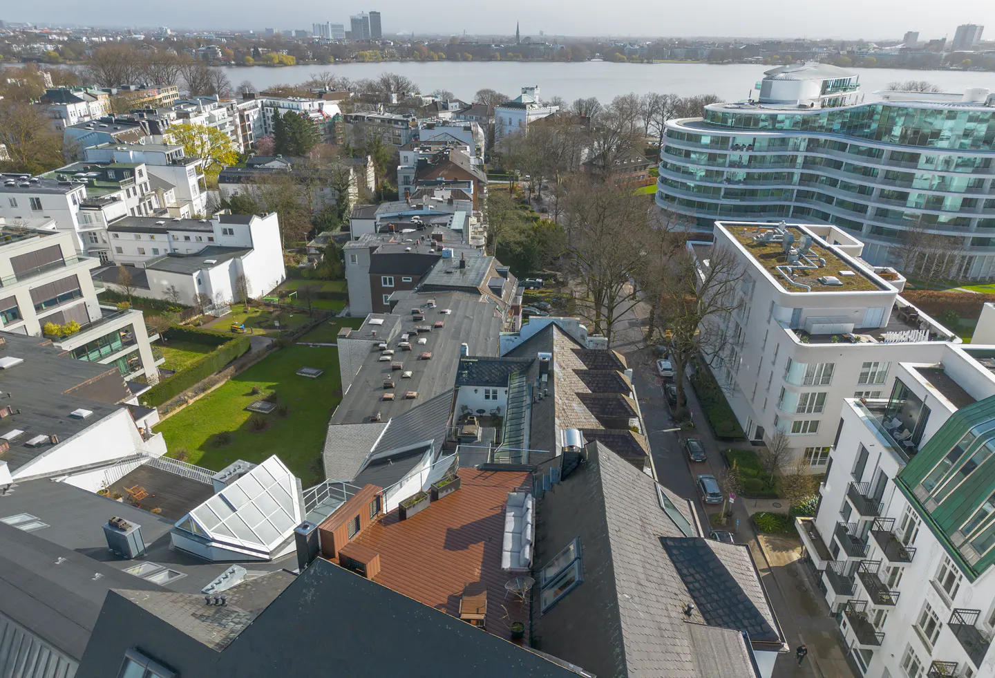 Aerial view of a Hamburg neighborhood with modern buildings, trees, and a lake in the background.