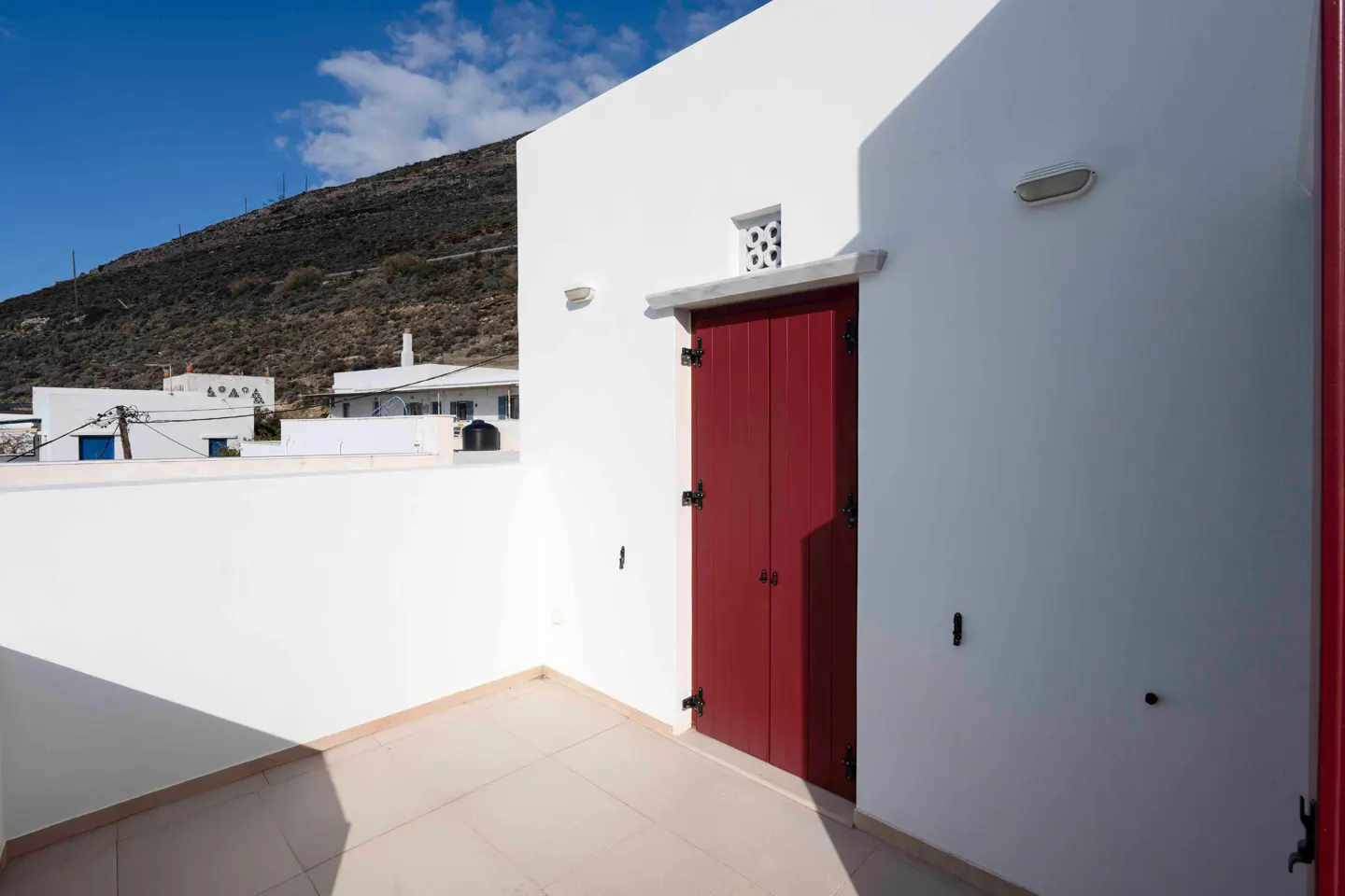 Exterior view of a white building with a red door and a mountain in the background.