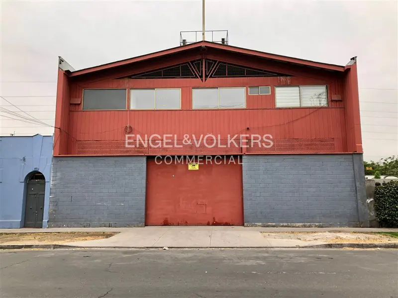 Exterior of a red commercial building with a gray brick base and a large red garage door. Engel & Volkers Commercial logo is visible.