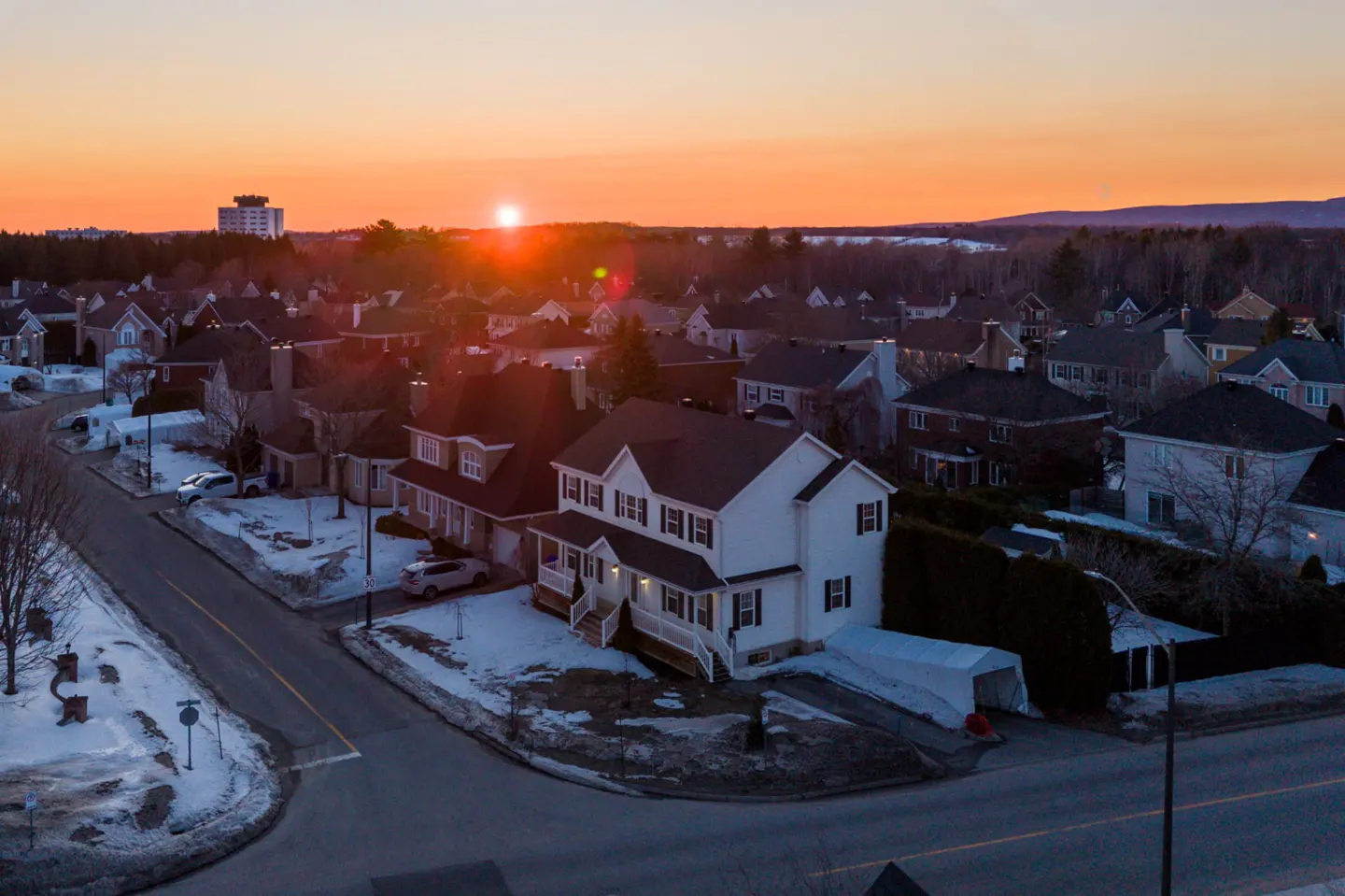 Aerial view of a two-story white house with black shutters at sunset in a suburban neighborhood with snow on the ground.