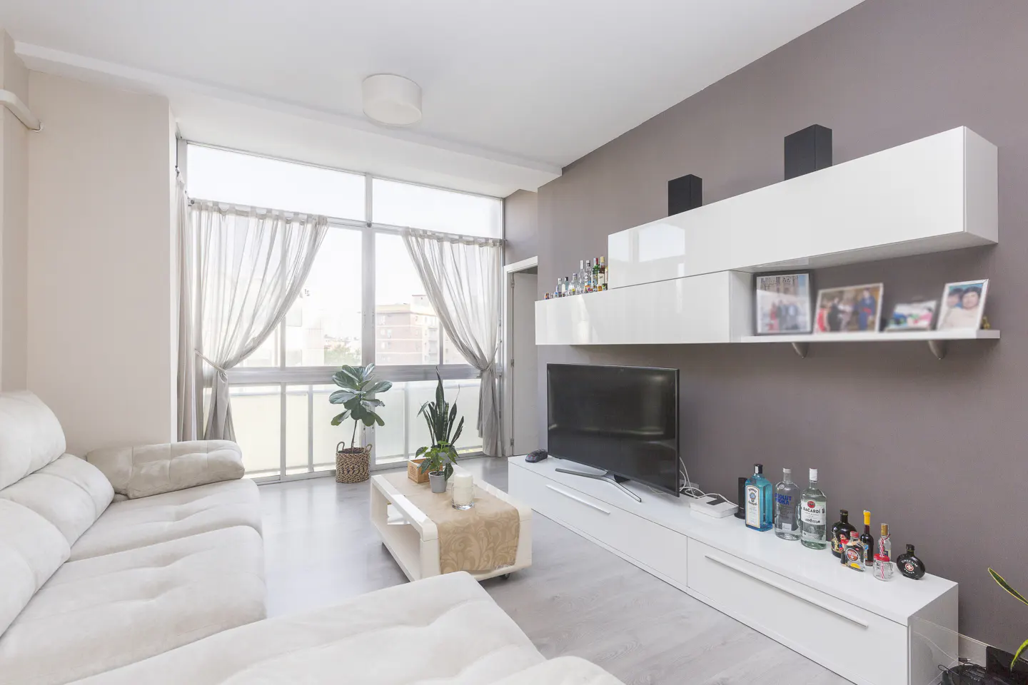 Modern living room with a white sectional sofa, a coffee table, and a wall-mounted white media unit with a flat-screen TV.