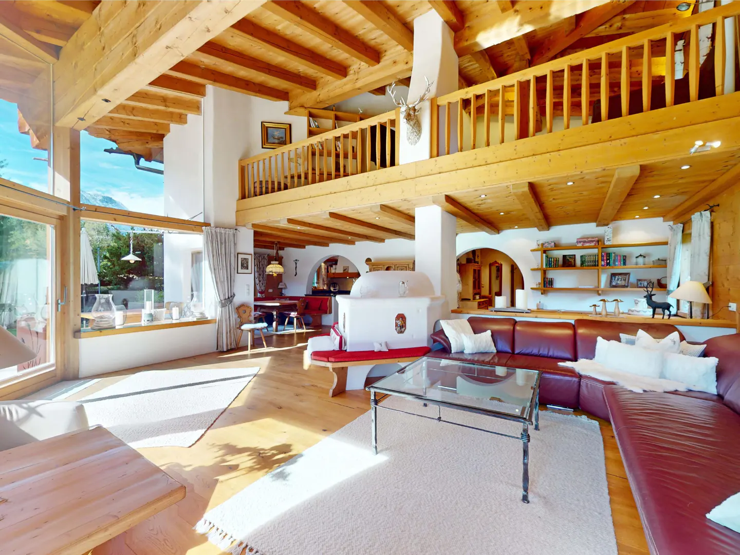 Living room with wood beams, a leather couch, and a glass coffee table. A deer head is mounted above the fireplace.