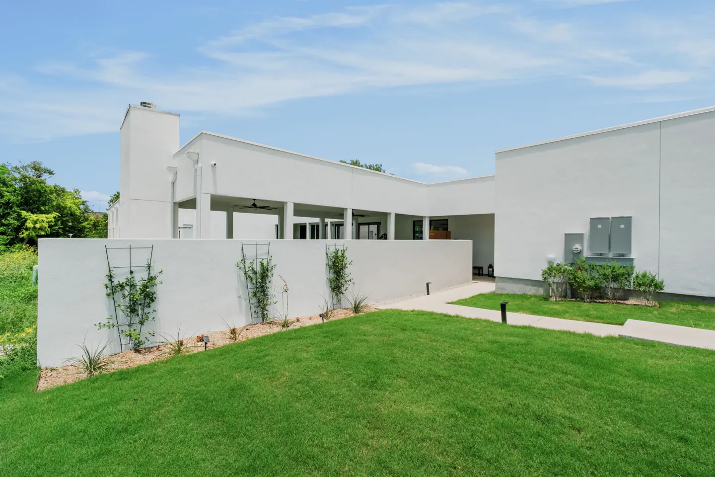 Modern white home with a flat roof, covered patio, and a green lawn with a walkway under a bright blue sky.
