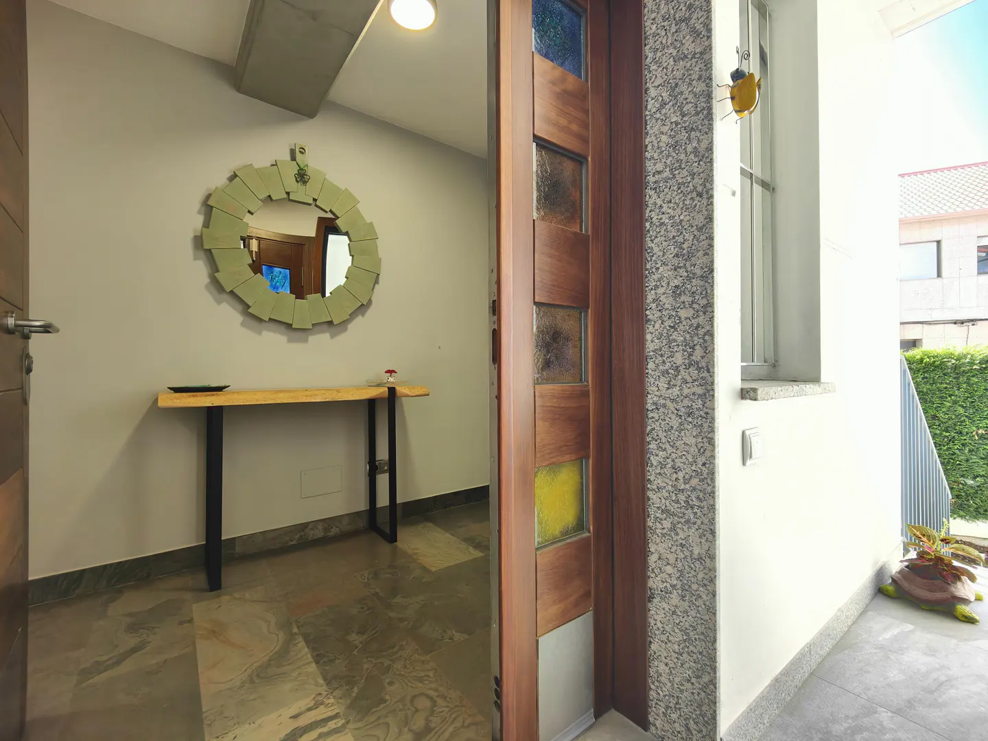 Open wooden front door with stained glass panels, leading to a foyer with a round mirror, table, and marble floor.