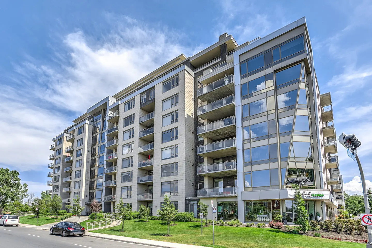 Modern condo building with glass balconies and reflective windows under a blue sky.