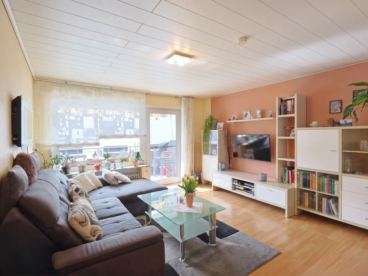 Living room with brown sectional sofa, glass coffee table with tulips, and white entertainment center with TV.