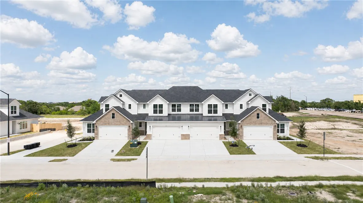 New white townhouses with brick accents and black roofs under a cloudy blue sky.
