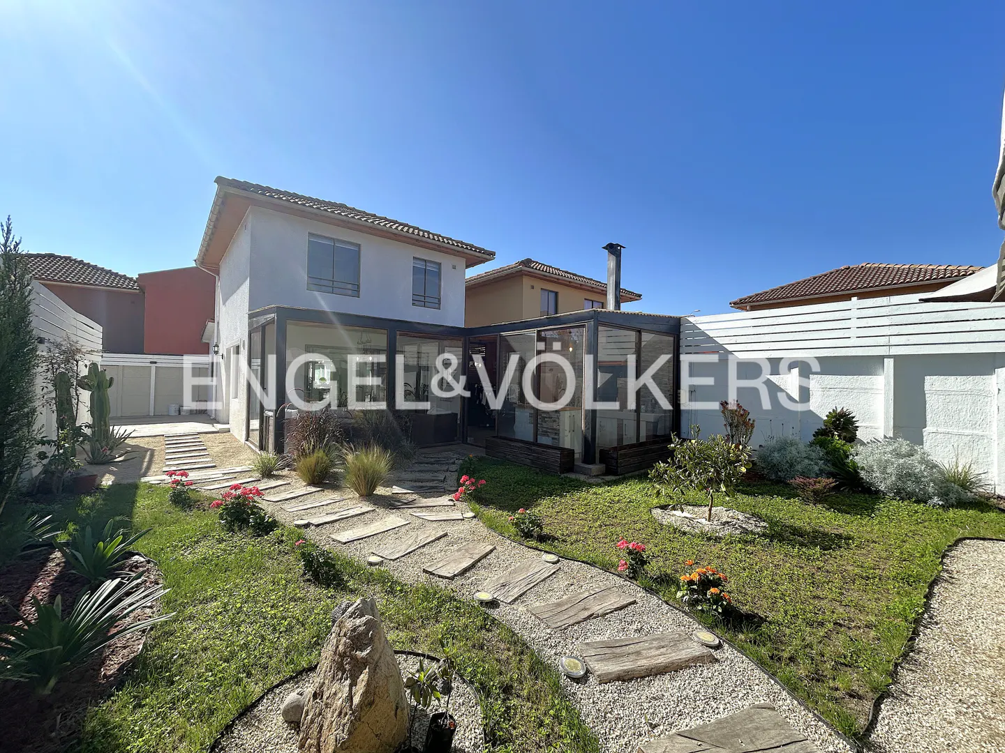 Backyard of a two-story white house with a glass-enclosed patio, stone path, green lawn, and white privacy fence.