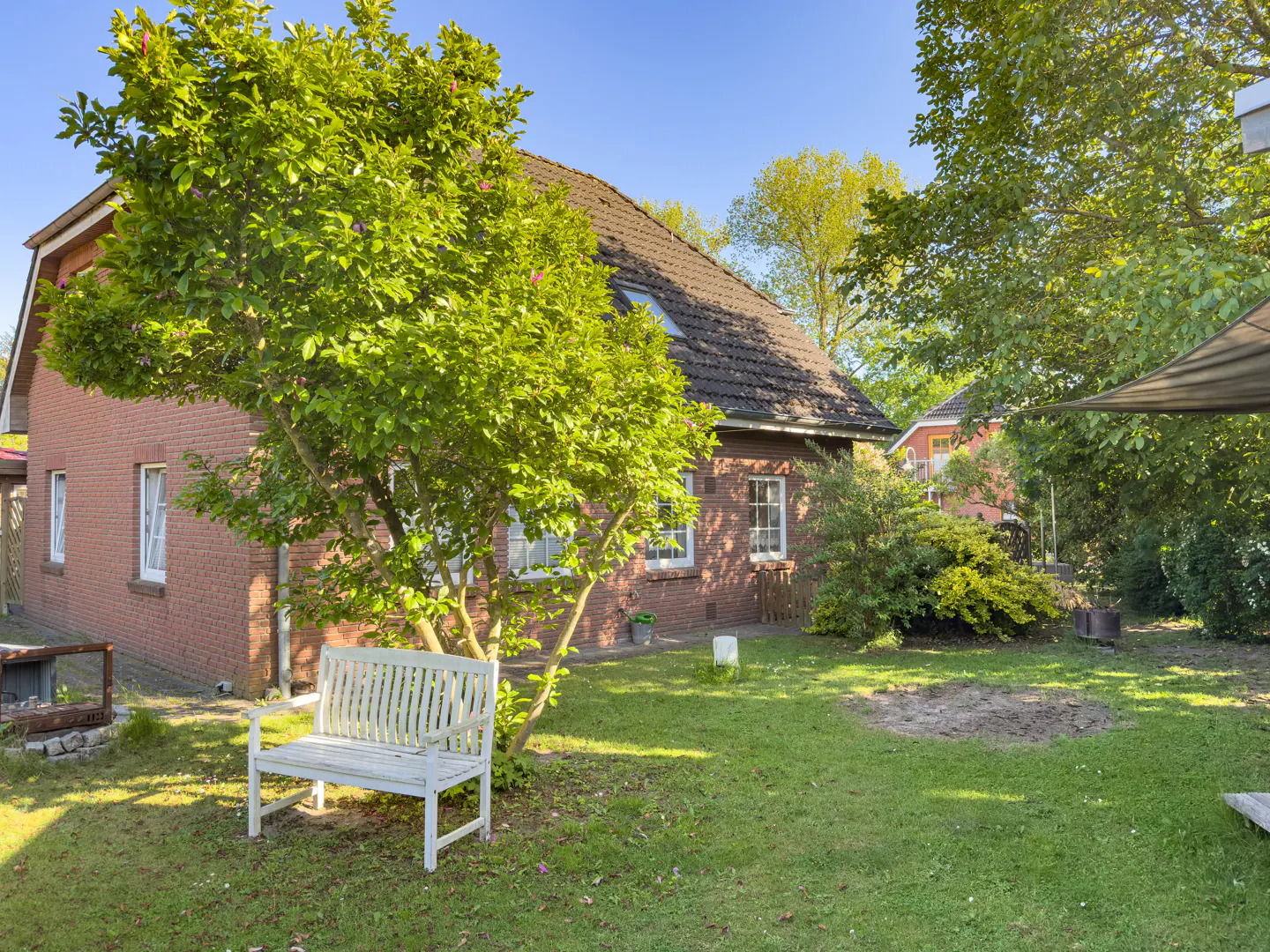 Brick house with a white bench in the yard. Green grass and trees surround the house. Blue sky above.