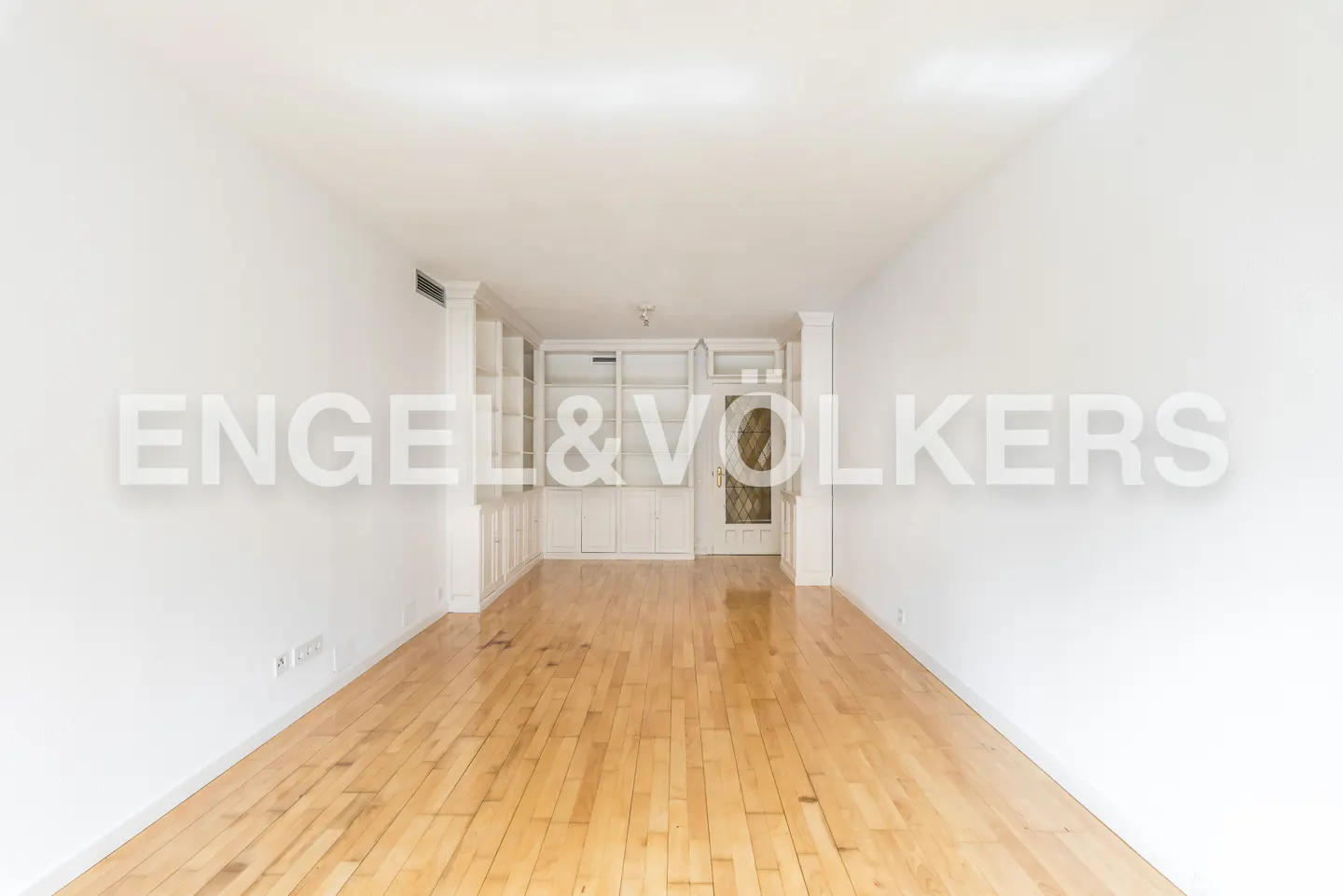 Empty room with hardwood floors, white walls, and built-in white shelving and cabinets. A glass-paneled door is centered in the back.