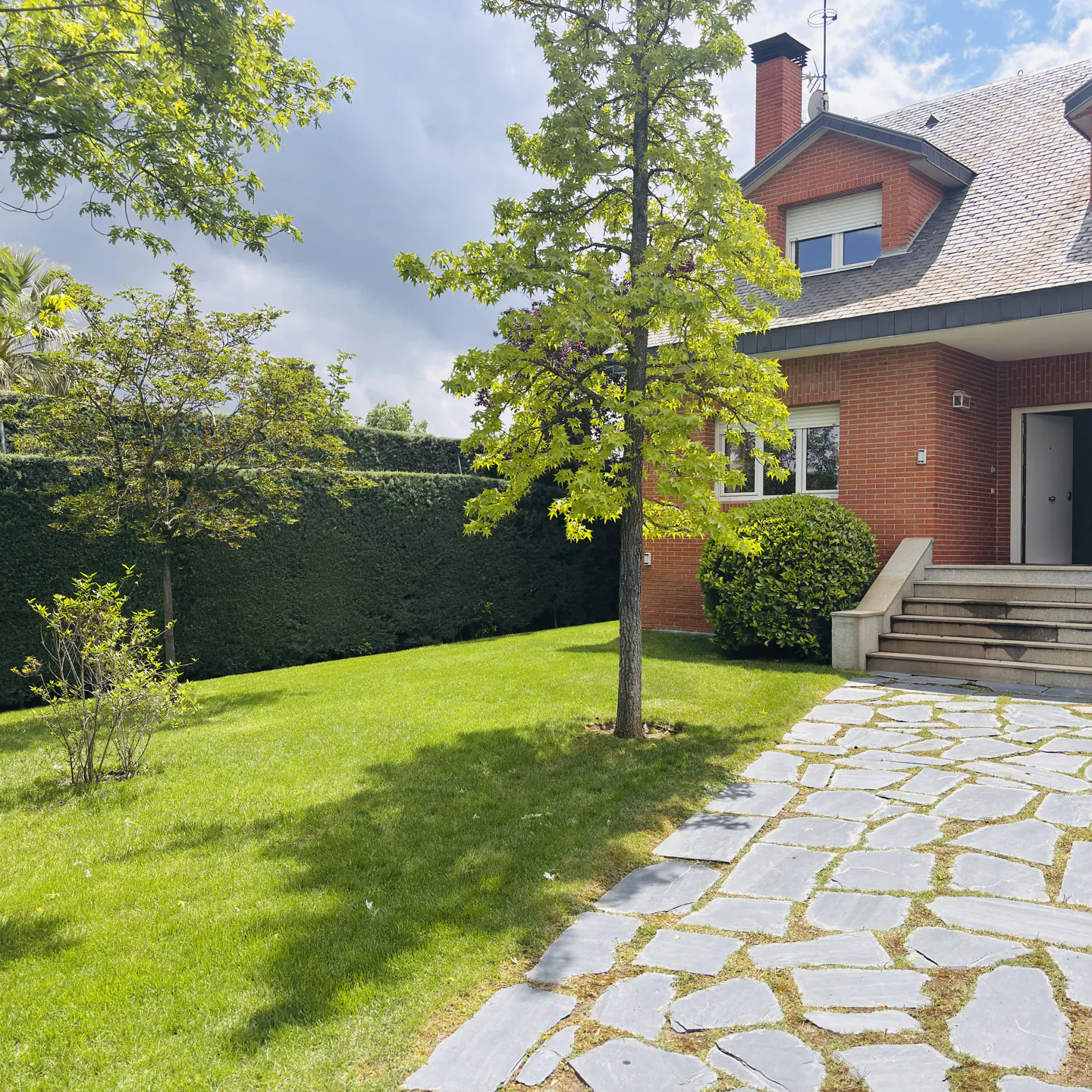 Exterior view of a red brick house with a green lawn, trees, and a stone walkway leading to the front door.