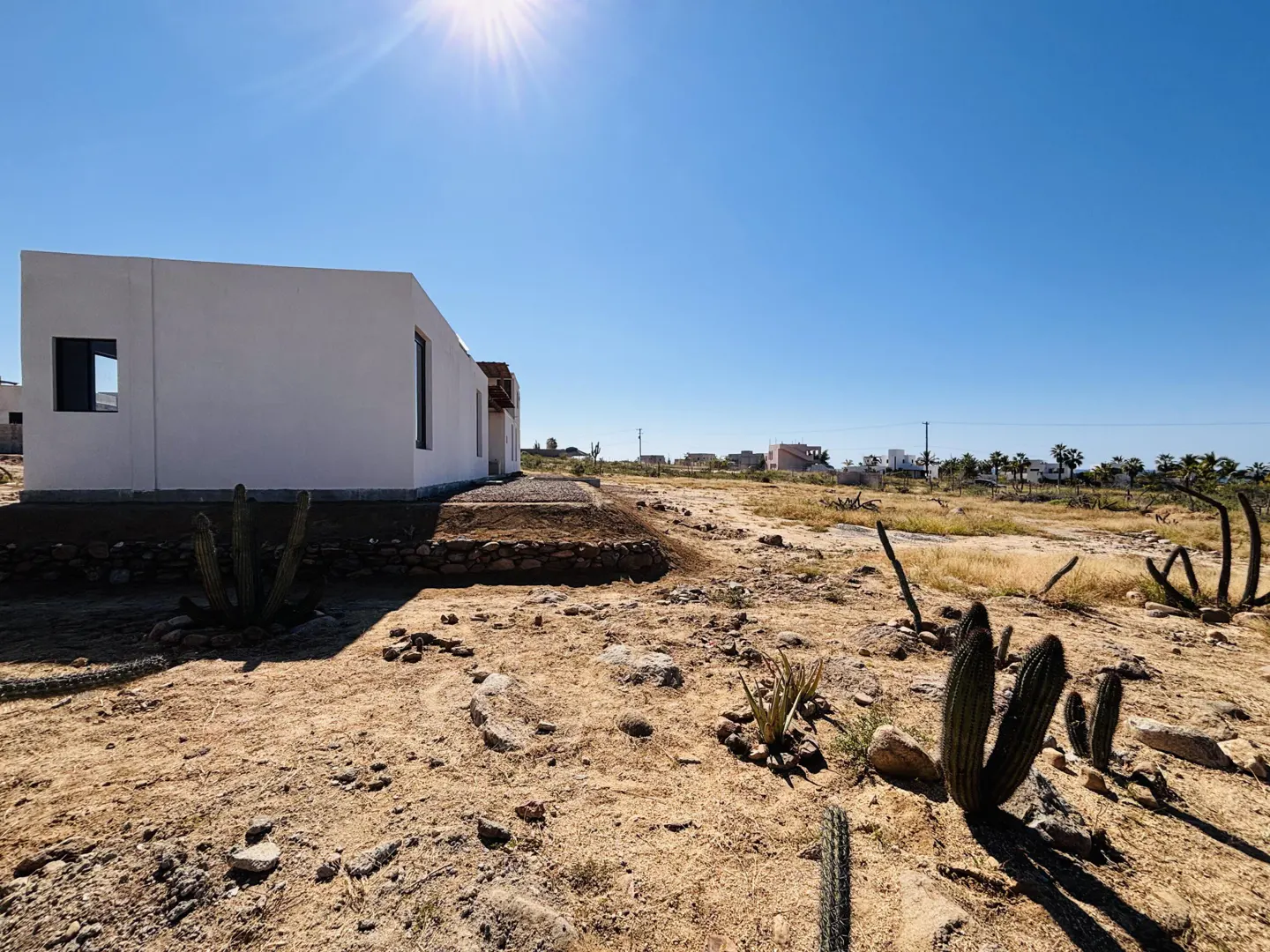 A white, modern house sits in a desert landscape under a clear blue sky with cacti.