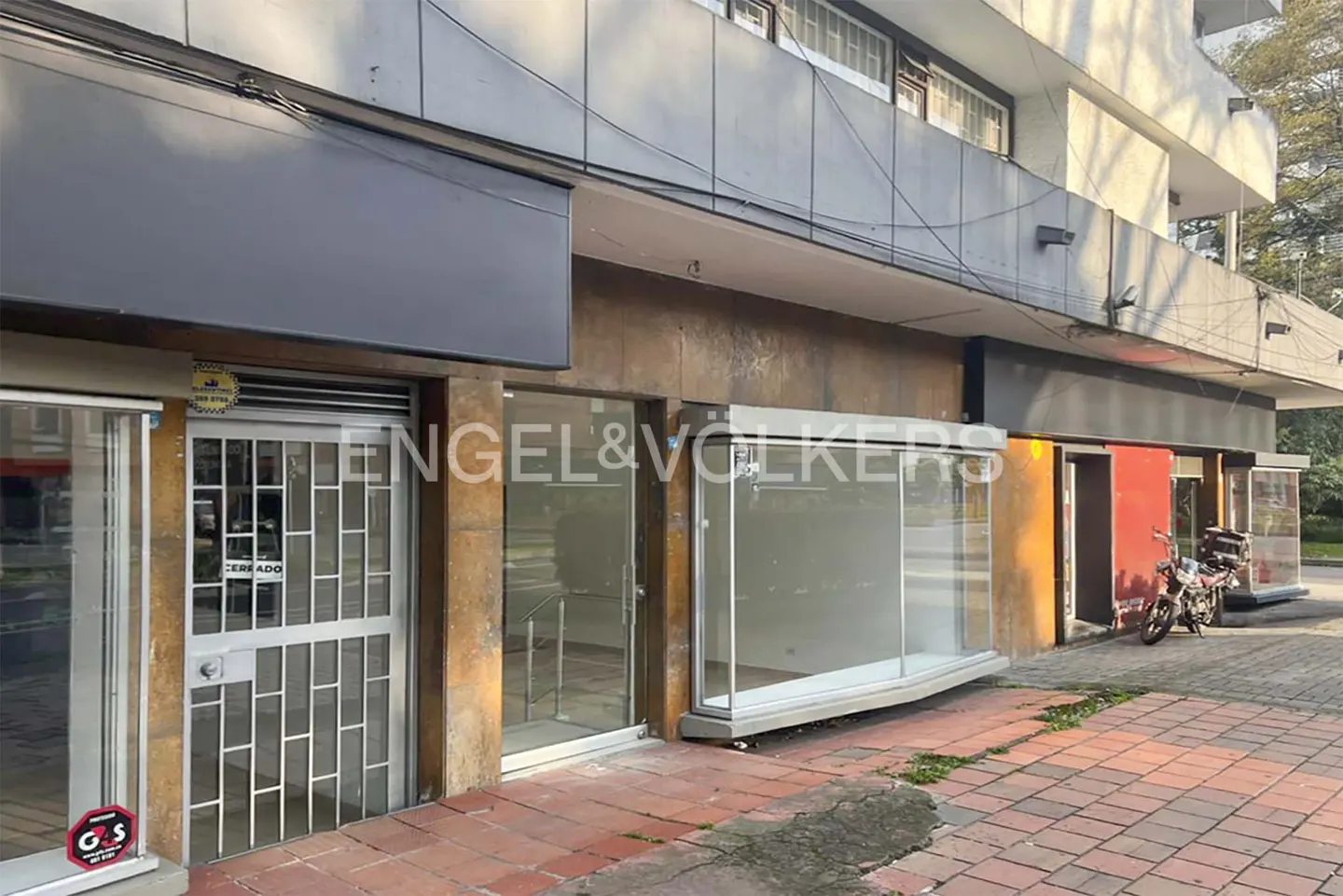 Engel & Völkers storefront with glass windows and a metal security gate. A motorcycle is parked on the sidewalk.