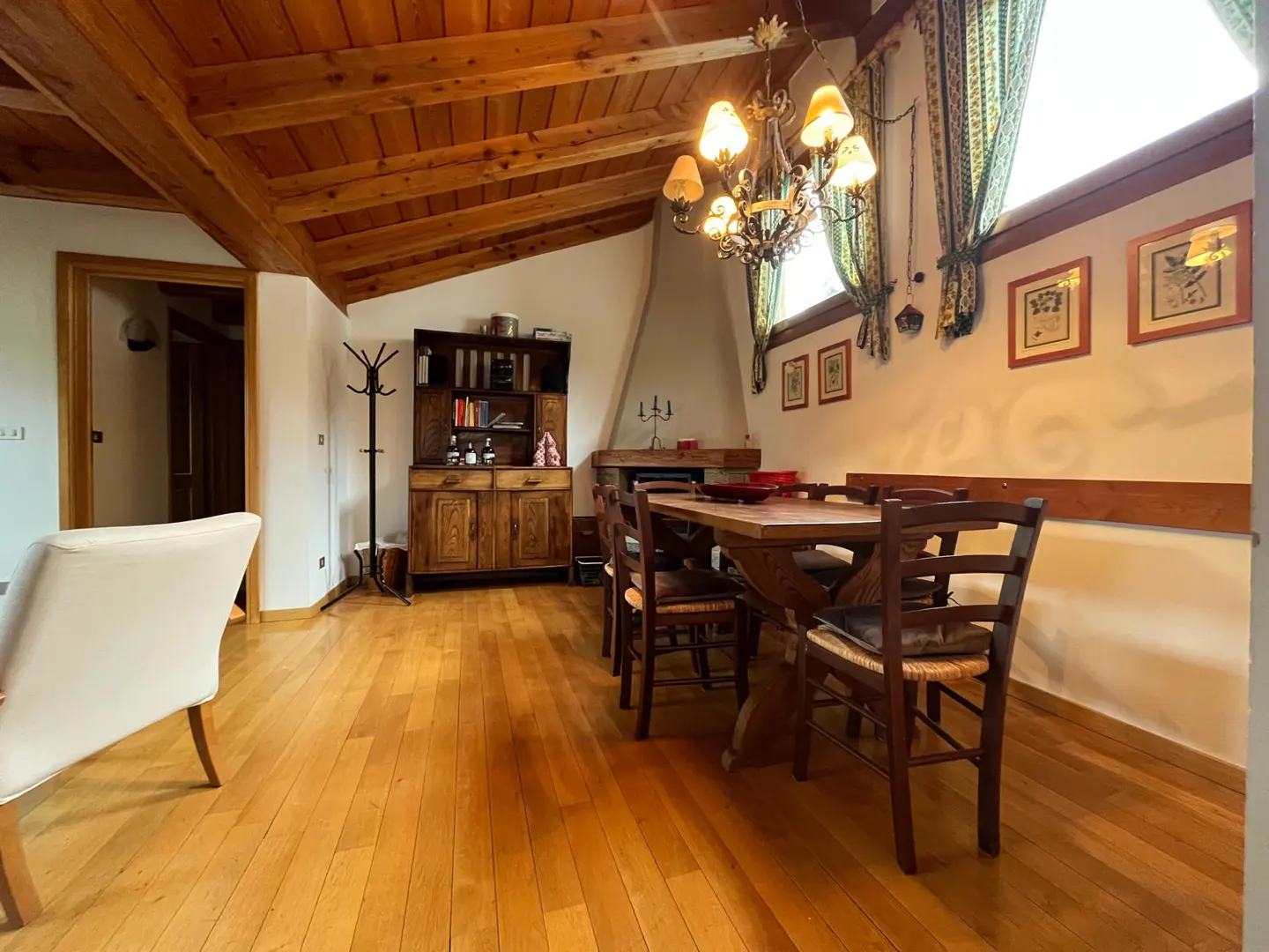Dining room with wooden floors, vaulted ceiling, rustic table and chairs, chandelier, and a fireplace in the background.