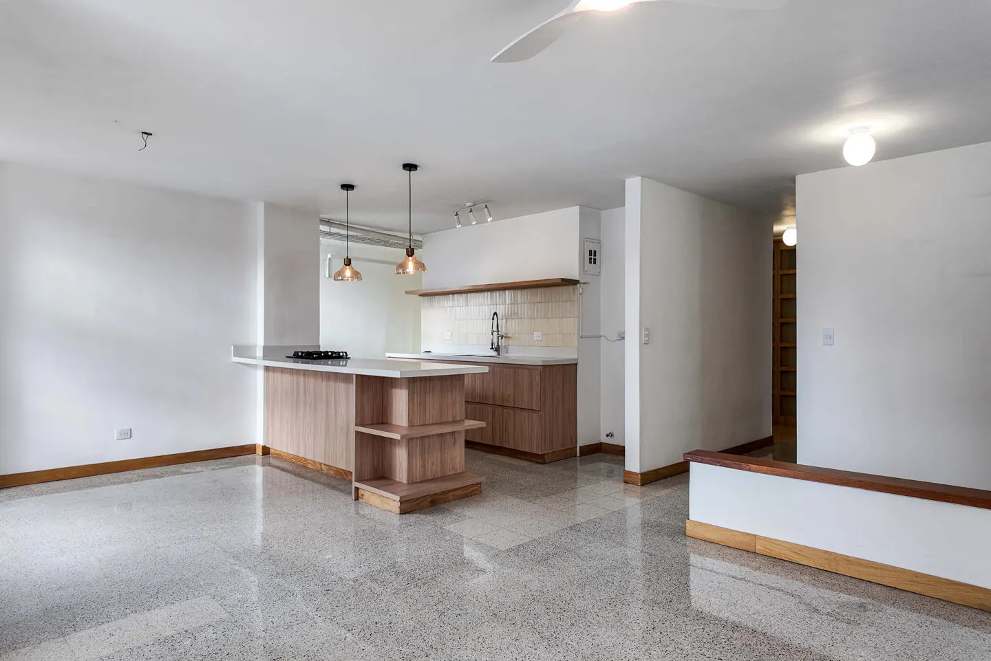 Open-concept apartment with white walls, terrazzo floors, and a kitchen island with wood cabinets and a white countertop.