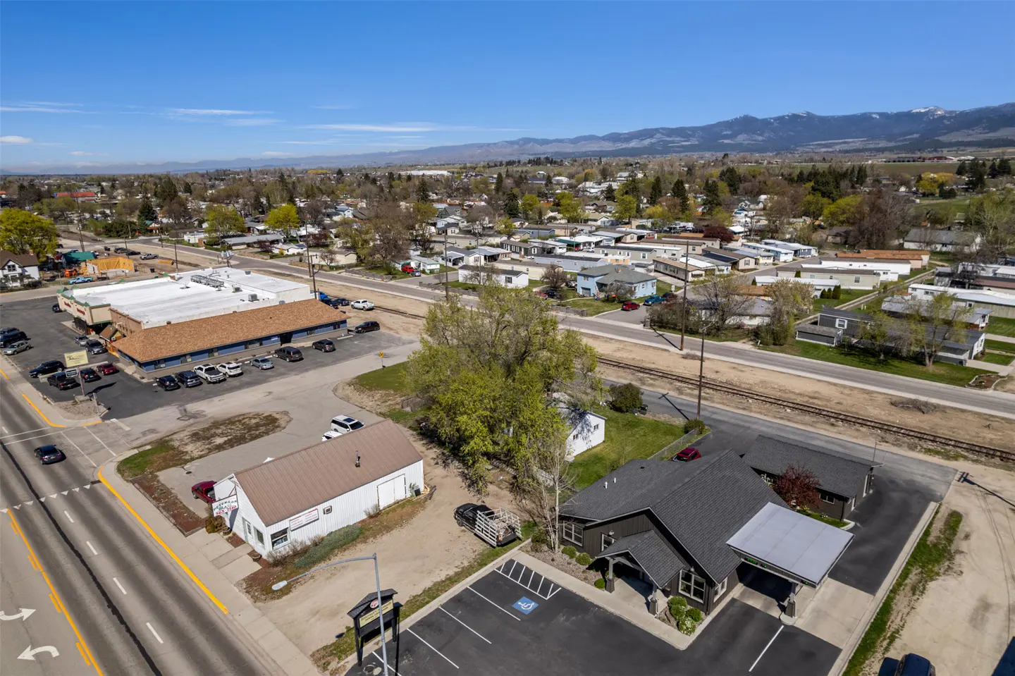 Aerial view of a commercial property with a dark gray building, parking lot, and street. Mountains are visible in the background.