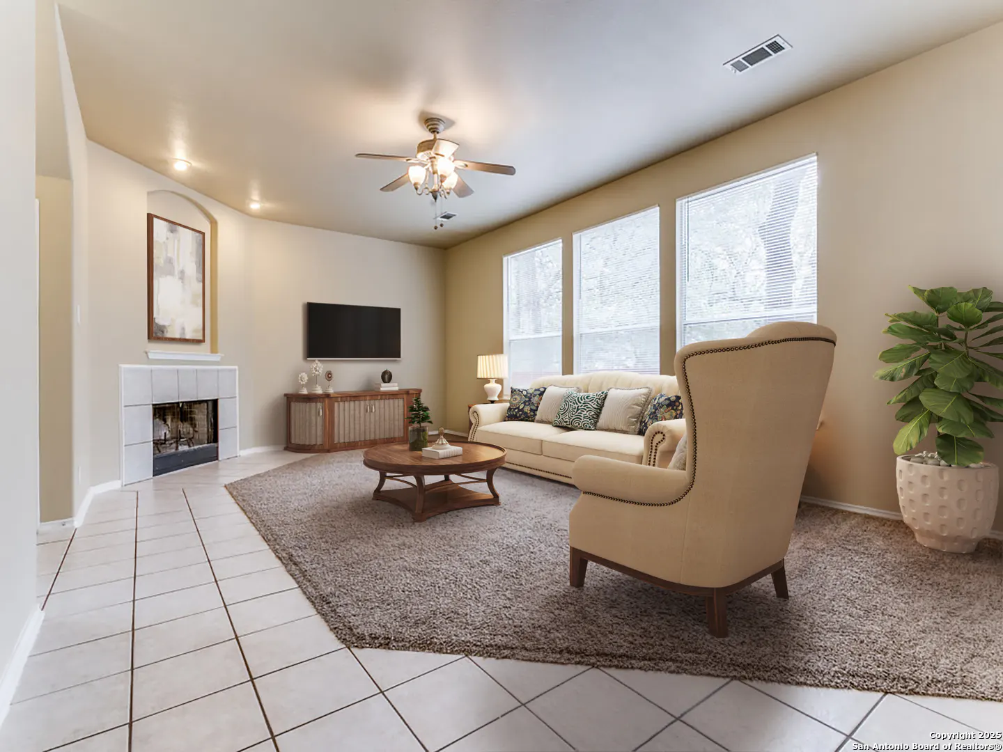 Living room with beige walls, tile floors, and a brown rug. A cream sofa, chair, and wood furniture are arranged around a coffee table. A fireplace and TV are on the wall.