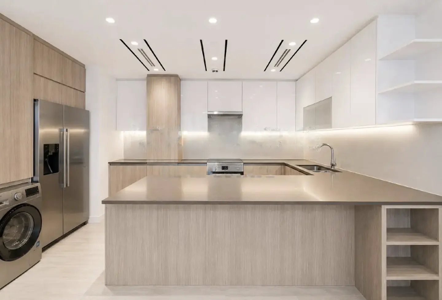 Modern kitchen with light wood cabinets, white upper cupboards, stainless steel appliances, and a large central island.