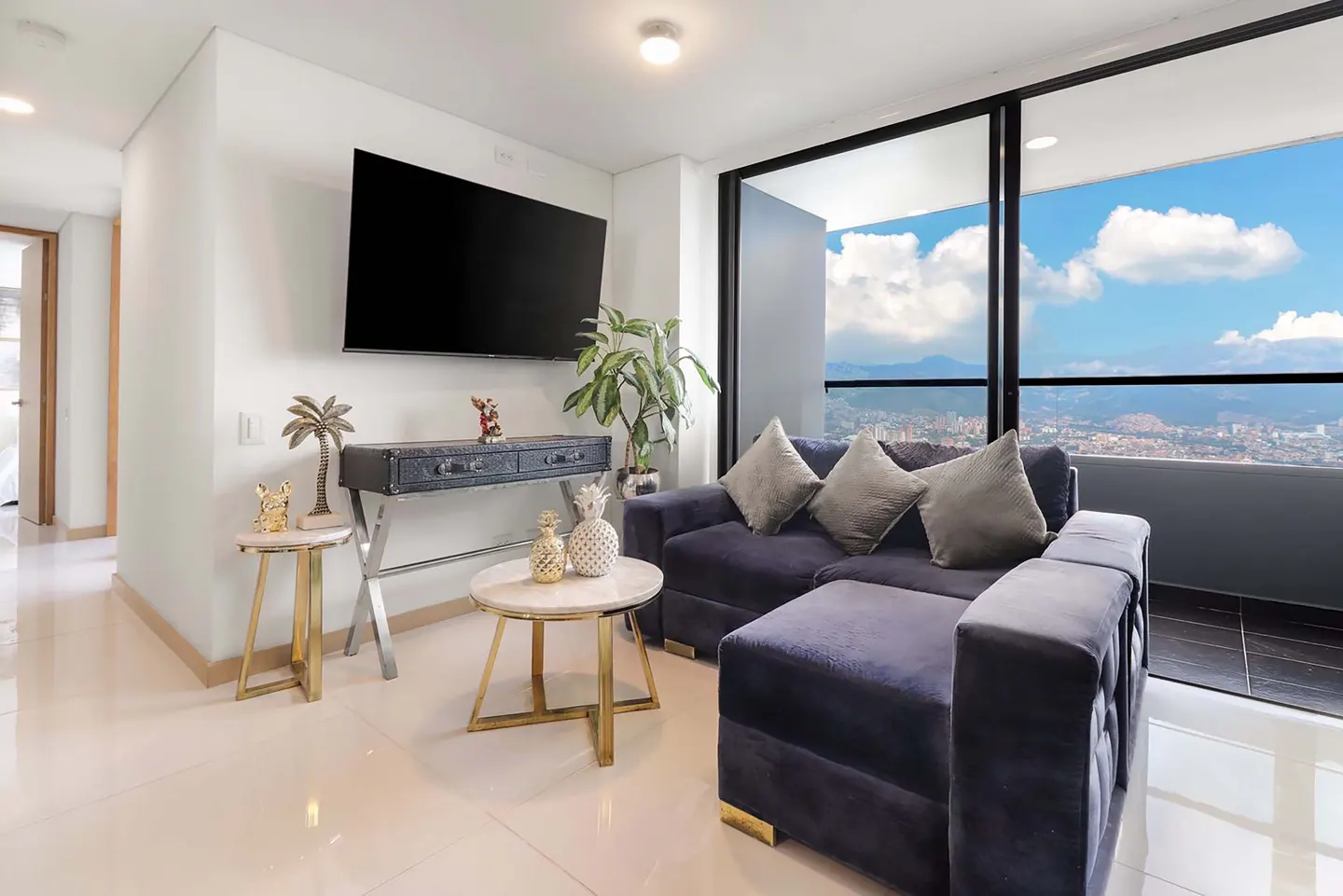 Bright living room with a navy sectional sofa, a black TV, and a city view through a large window.