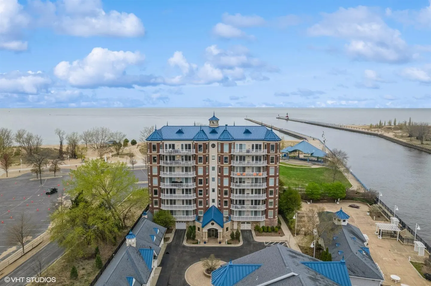 Aerial view of a brick condo building with blue roof, balconies, and lakefront access on a cloudy day.