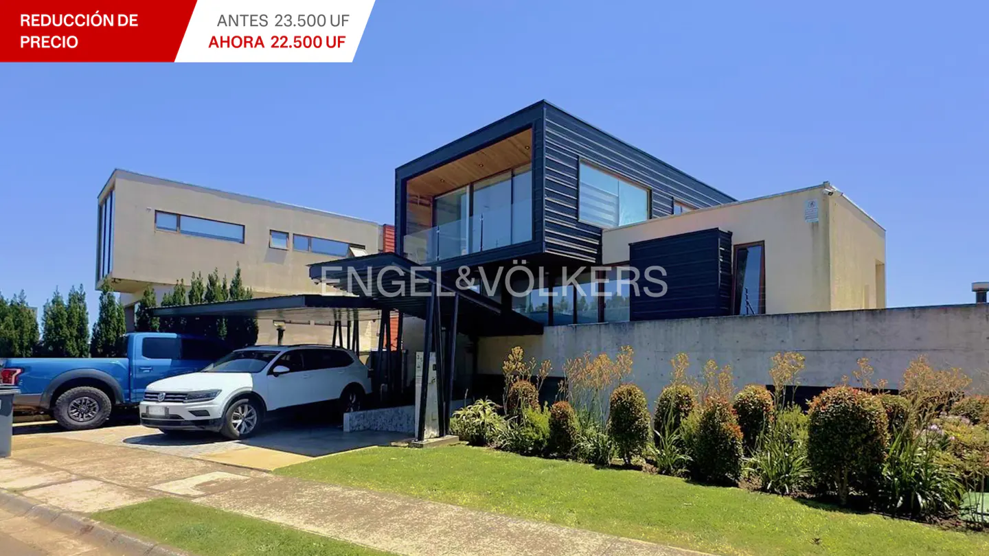 Modern two-story home with a black frame, glass balcony, and a carport with a white SUV and blue truck.