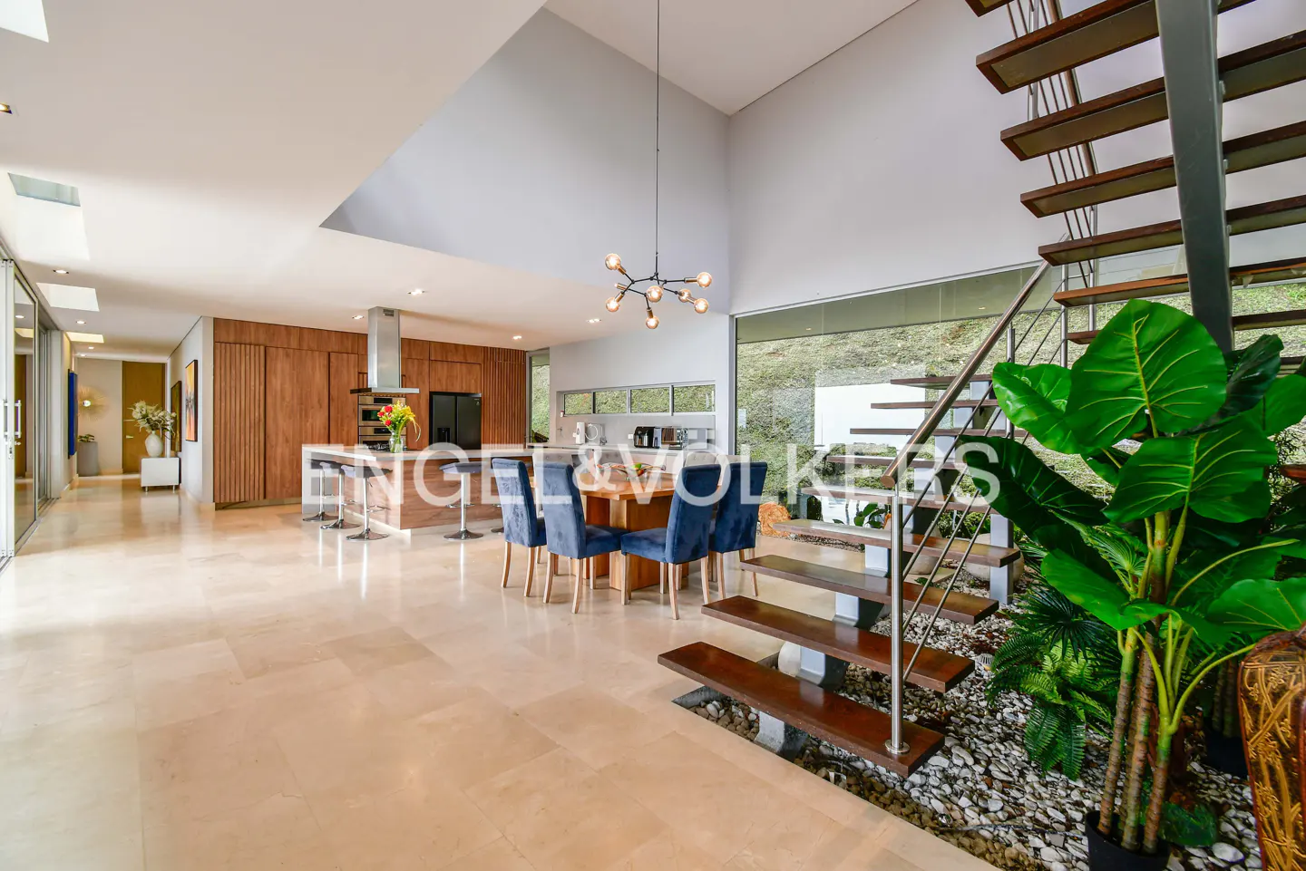 Open-concept living space with a kitchen island, dining table, and staircase with indoor plants.