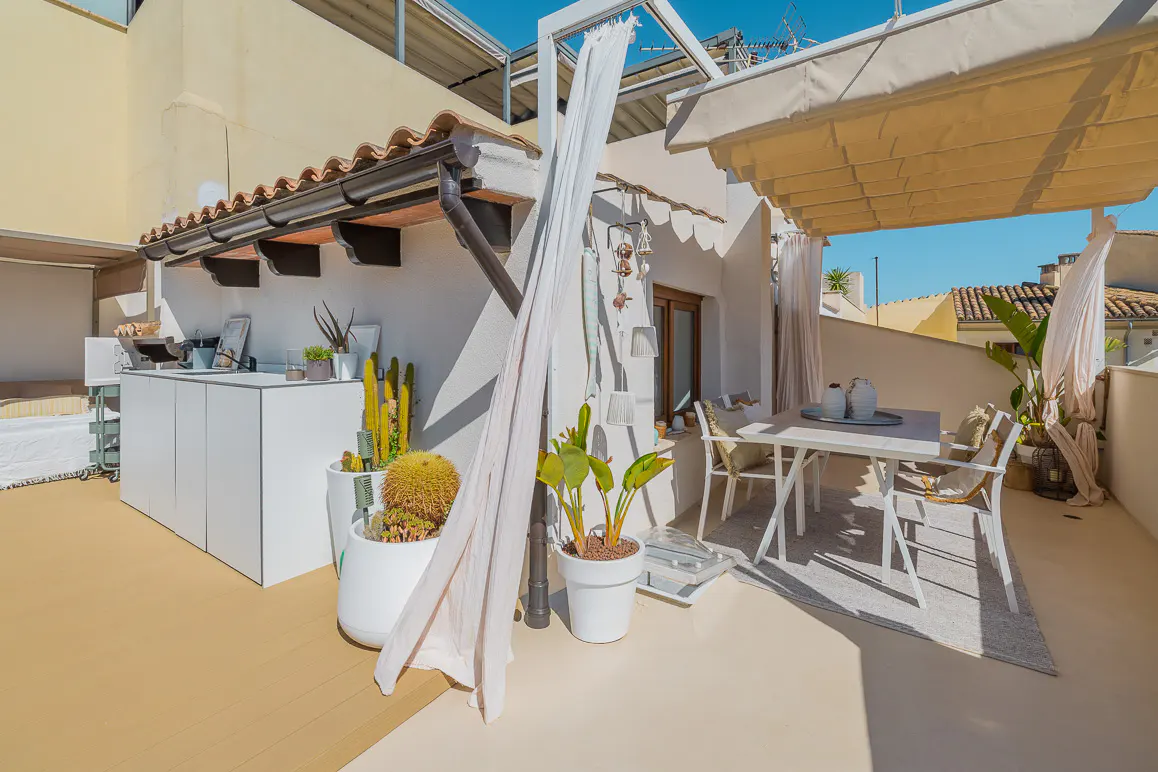 A bright rooftop terrace with white furniture, potted plants, and a retractable awning.