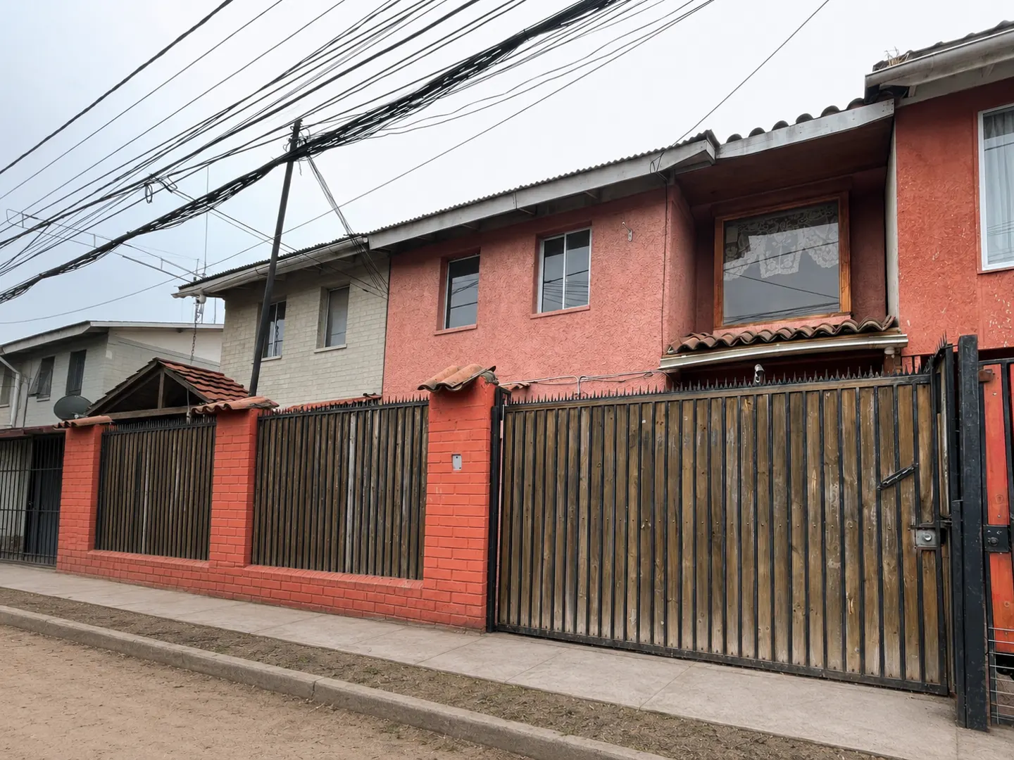 Row of colorful two-story houses with brick and wood fences under a cloudy sky.