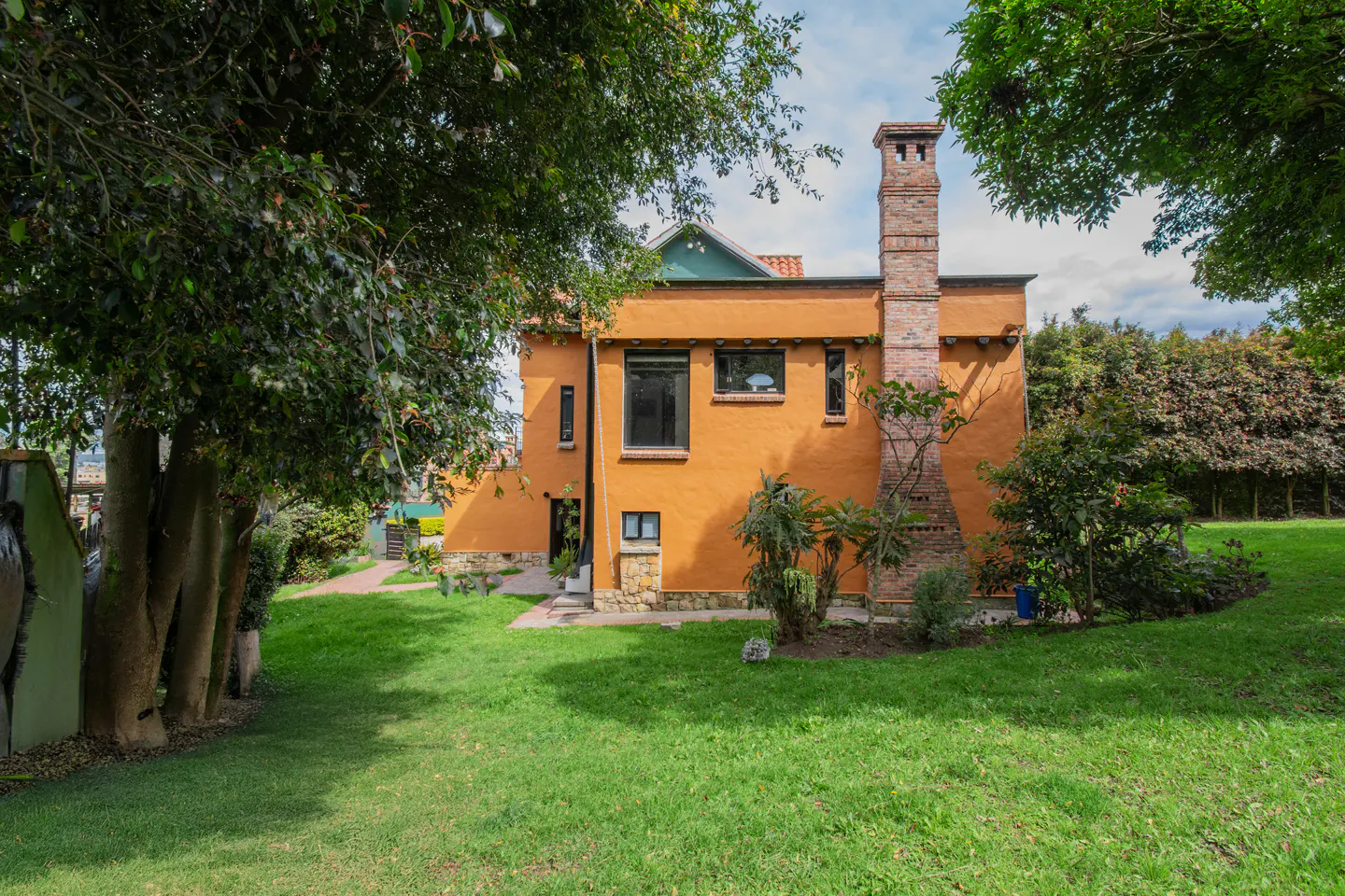 Exterior view of a two-story orange house with a brick chimney, surrounded by green trees and a lawn.
