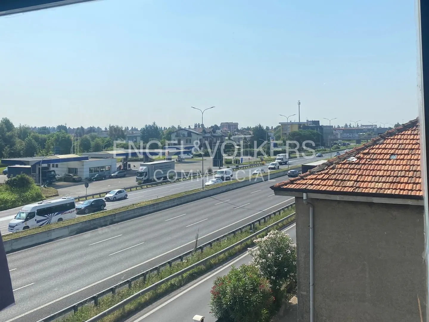 View of a busy highway with cars and trucks, with buildings and trees in the background. Engel & Volkers logo is visible.